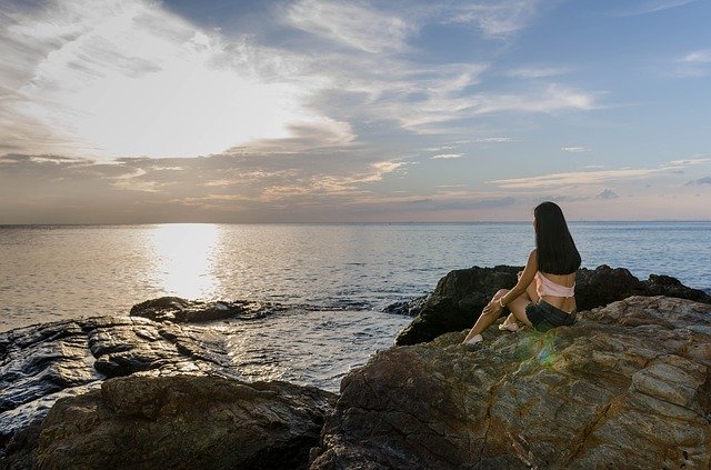 Žena sedí na skalách pri mori v zátoke za súmraku.jpg