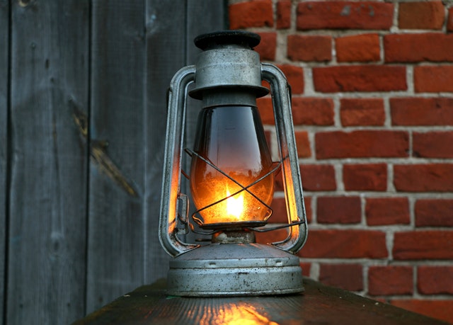 Lampáš so zapálenou sviečkou pri tehlovej stene a drevených dverách 